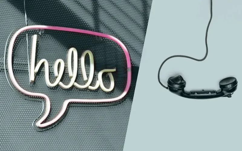 Neonschild "Hallo" in einer Sprechblase auf der linken Seite; alter Telefonhörer mit Schnur auf der rechten Seite, vor einem hellen Hintergrund.